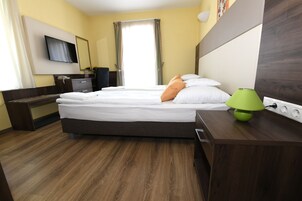 Habitación de hotel con cama, mesita de noche, lámpara y televisor montado en la pared.