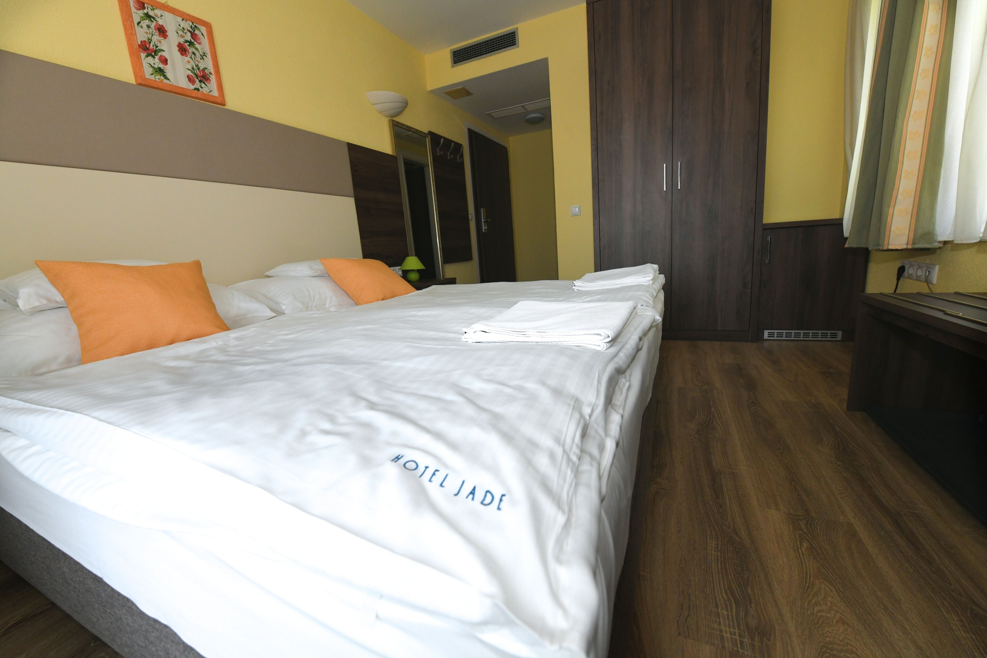 A hotel room with a large bed, two pillows, a nightstand, and a wooden floor.