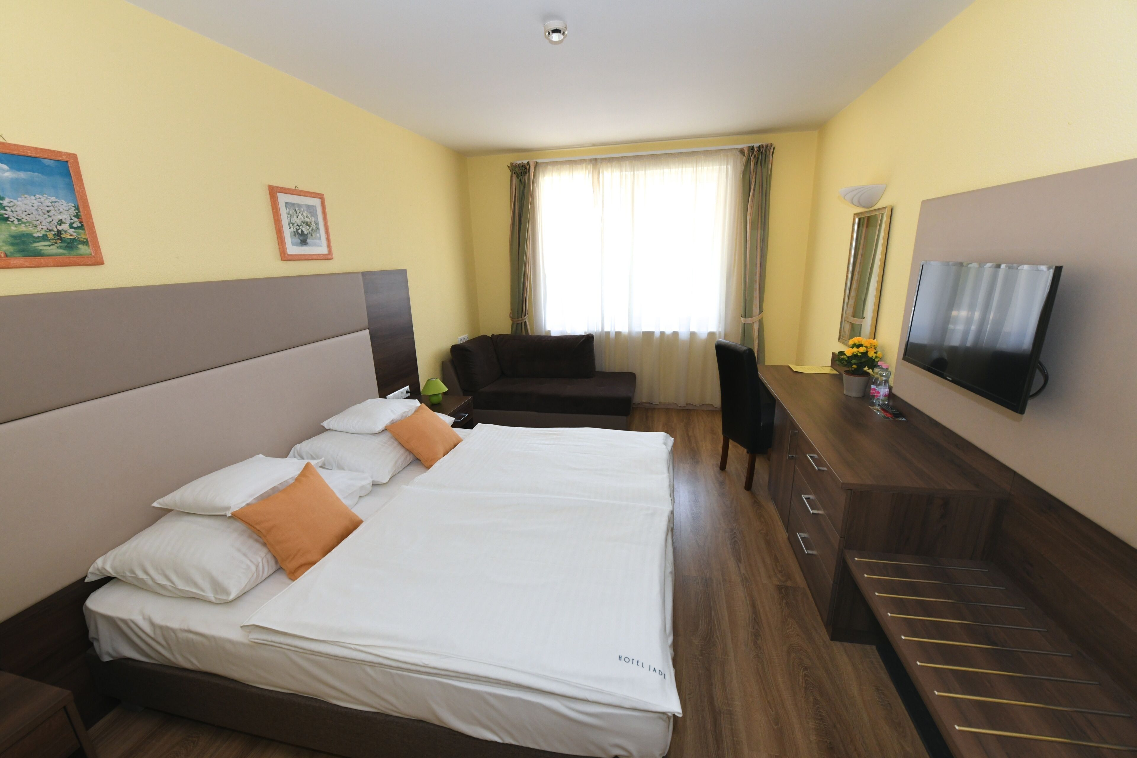 A hotel room with a large bed, a desk, a chair, a TV, and a window with curtains.