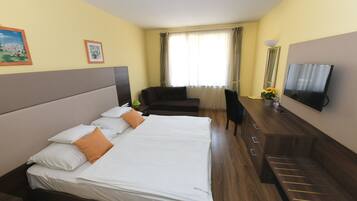 Habitación de hotel con una cama grande, un escritorio, una silla, un televisor y una ventana con cortinas.