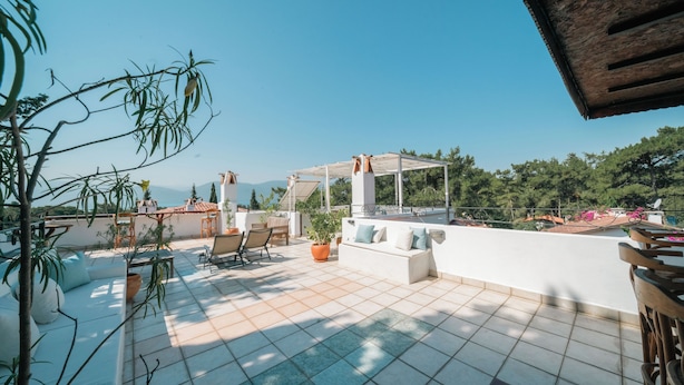 Eine Dachterrasse mit Sitzgelegenheiten im Freien, einer Pergola und Blick auf Meer und Berge.