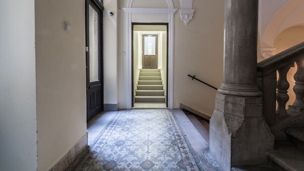 Un pasillo con piso estampado, una escalera que sube a un nivel superior y una columna con barandilla.