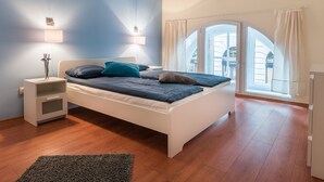 Un dormitorio con cama, mesitas de noche, cortinas y vistas a edificios.