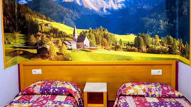 A room with two beds, a small table, and a mural of a mountainous landscape. - Pension Albor (Gijon)