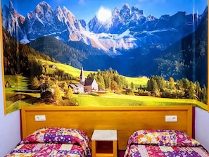 A room with two beds, a small table, and a mural of a mountainous landscape. - Pension Albor (Gijon)