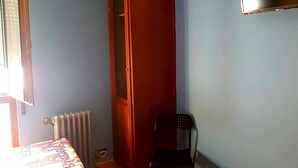 A room with a wooden wardrobe, a radiator, a chair, and a TV mounted on the wall. - Pension Albor (Gijon)