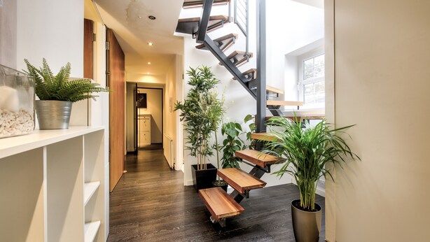 A modern staircase with wooden steps and metal railings, flanked by potted plants and a white shelving unit.