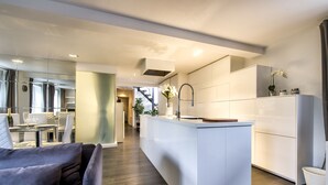 A modern kitchen with a central island, white cabinetry, and a dining area with a glass table and chairs.