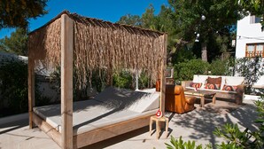 A wooden four-poster bed with a thatched roof, a wooden stool, and a sofa with cushions in a sunny outdoor setting. - Sunset Oasis Ibiza- Adults Only (Sant Josep de sa Talaia)