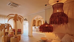 A spacious hotel lobby with a central seating area, a bar, and a large hanging light fixture. - Sunset Oasis Ibiza- Adults Only (Sant Josep de sa Talaia)
