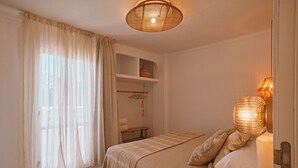 A bedroom with a bed, a bedside lamp, a shelf with a vase, and a window with sheer curtains. - Sunset Oasis Ibiza- Adults Only (Sant Josep de sa Talaia)