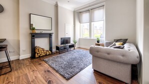 A living room with a fireplace, a television, a grey sofa, and a large window. - Stylish Modern Apartment Parking (Edinburgh)