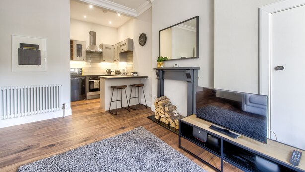 A modern kitchen with a central island, a dining area with bar stools, a fireplace, and a flat-screen TV. - Stylish Modern Apartment Parking (Edinburgh)