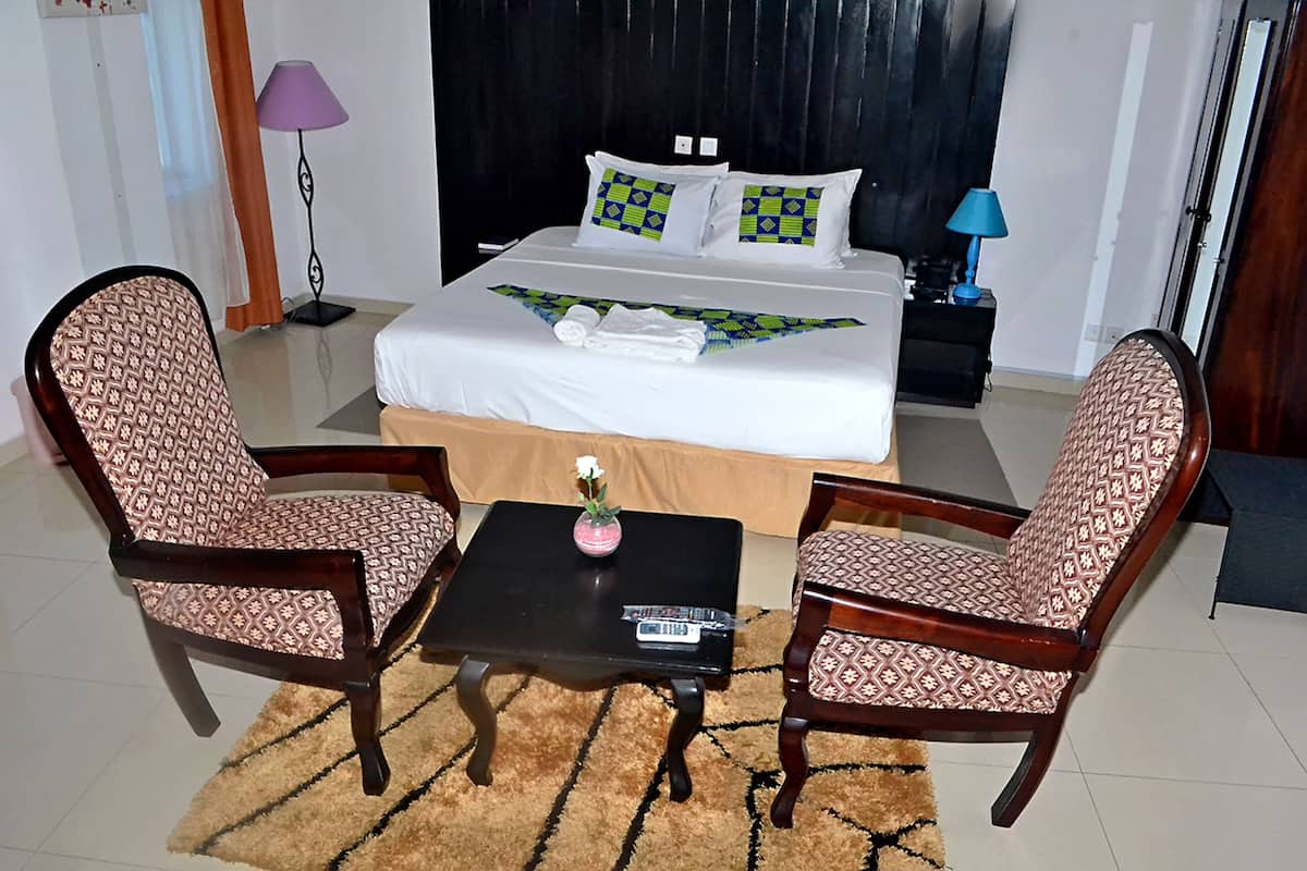 Una habitación de hotel con una cama, dos sillones con estampado, una mesita con un florero y una mesita de noche con lámparas.