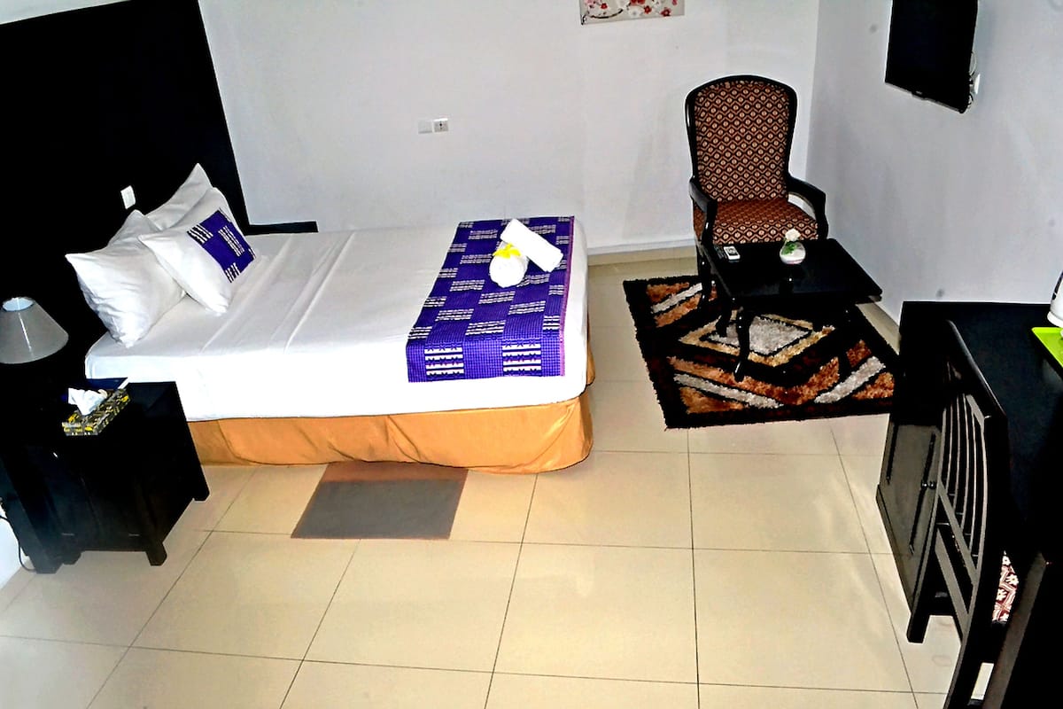 Una habitación de hotel con cama, una silla, una mesita y un televisor montado en la pared.
