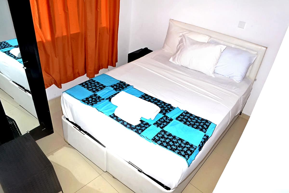 Una cama bien hecha con un cabecero blanco, una colcha de diseño azul y negro, y almohadas blancas.