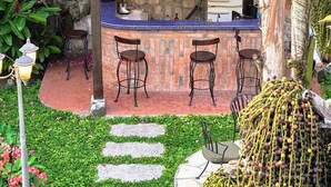 Un área de bar rústica al aire libre con techo de lámina corrugada, tres taburetes de bar y un muro de piedra de fondo.