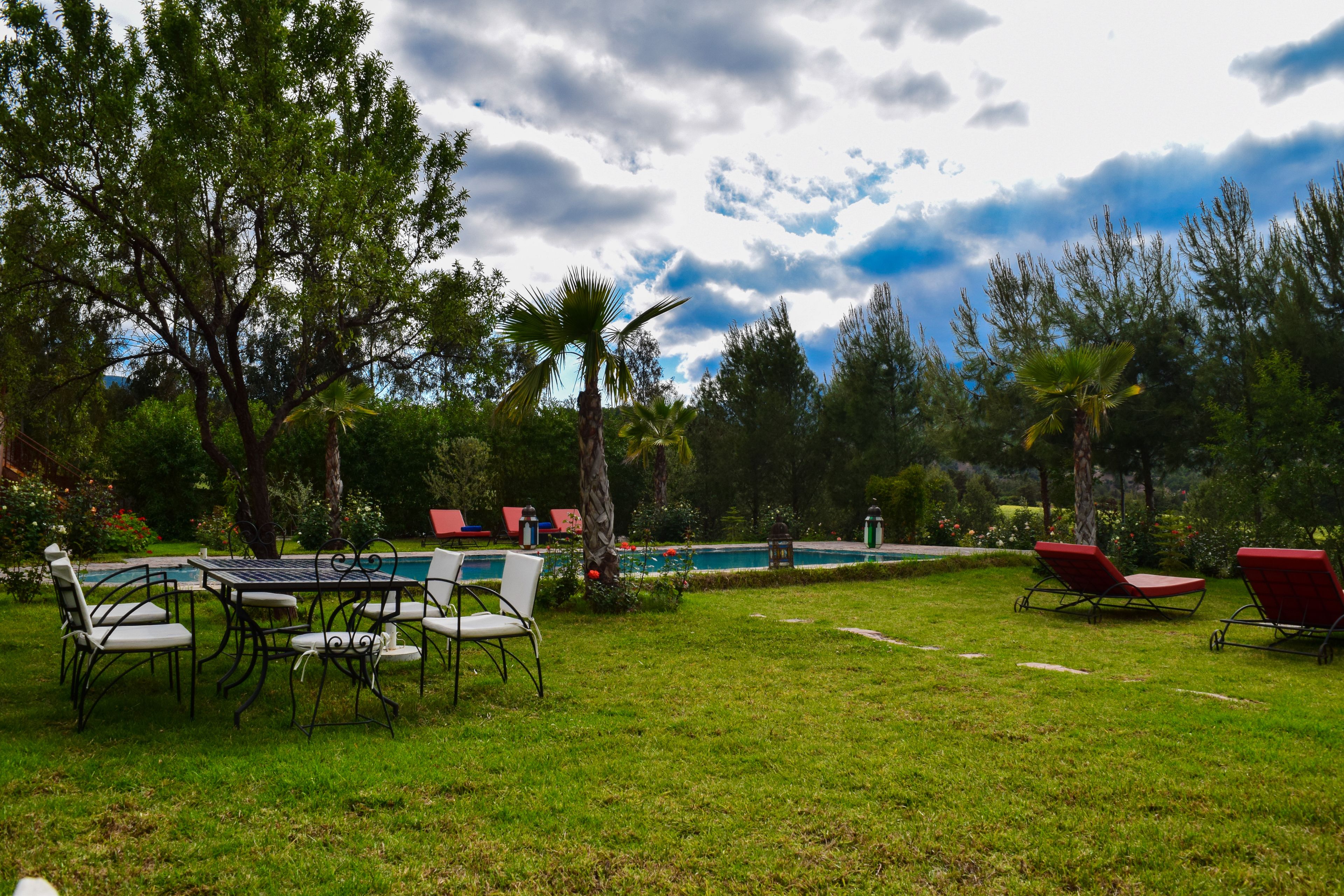 A pool area with lounge chairs and a dining table surrounded by trees.