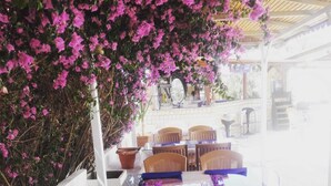 Un espace extérieur aménagé avec des chaises et des tables en osier, entouré de fleurs de bougainvillier roses.