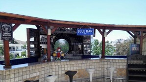 Un espace bar avec une enseigne bleue portant l’inscription « BLUE BAR », un chapeau décoratif pour le barman, et une vue sur la ville en arrière-plan.