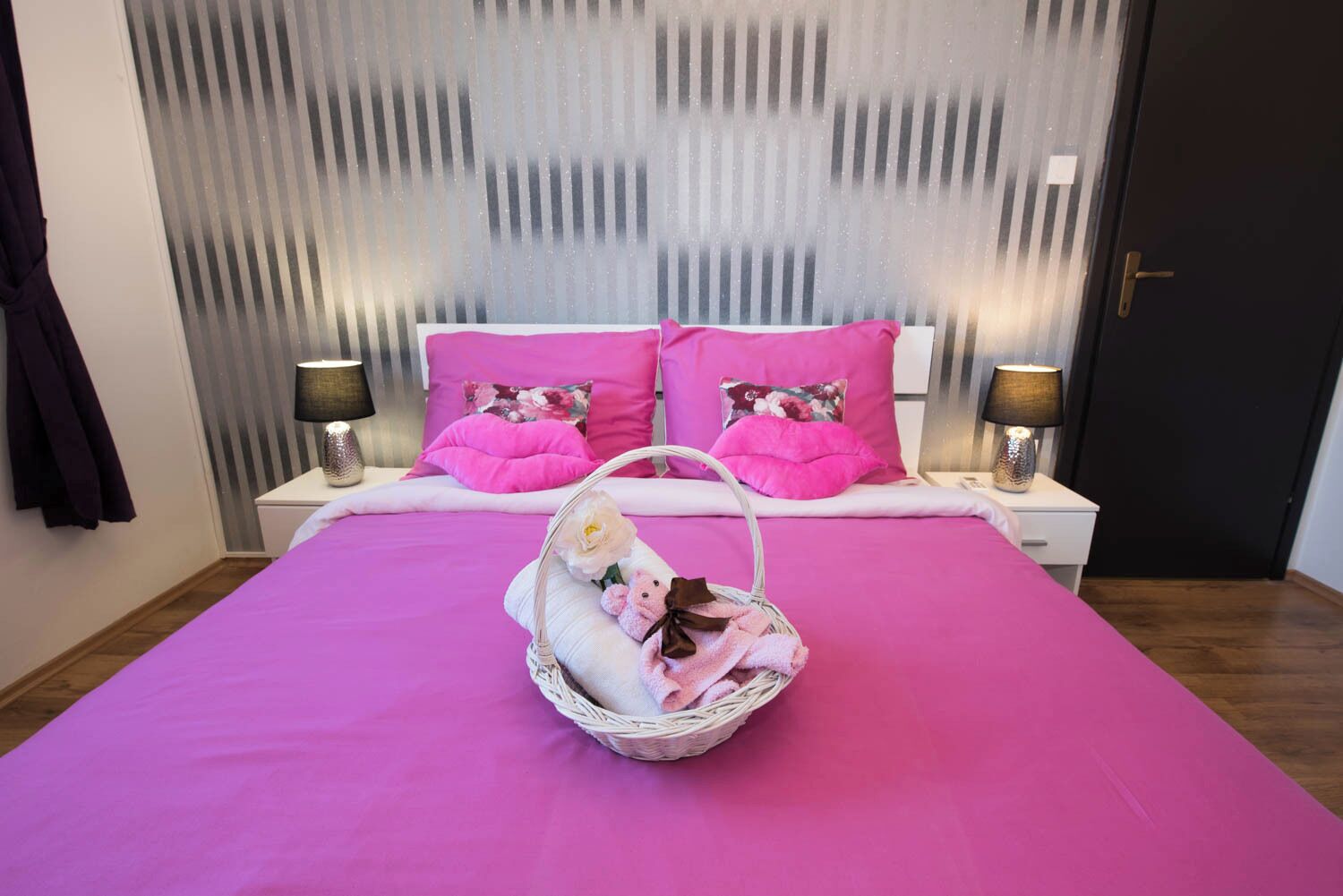 A bedroom with a bed, two nightstands, and a wall with vertical blinds.