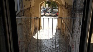 Un estrecho callejón con una reja metálica, suelo de baldosas y una calle visible a través de la reja.