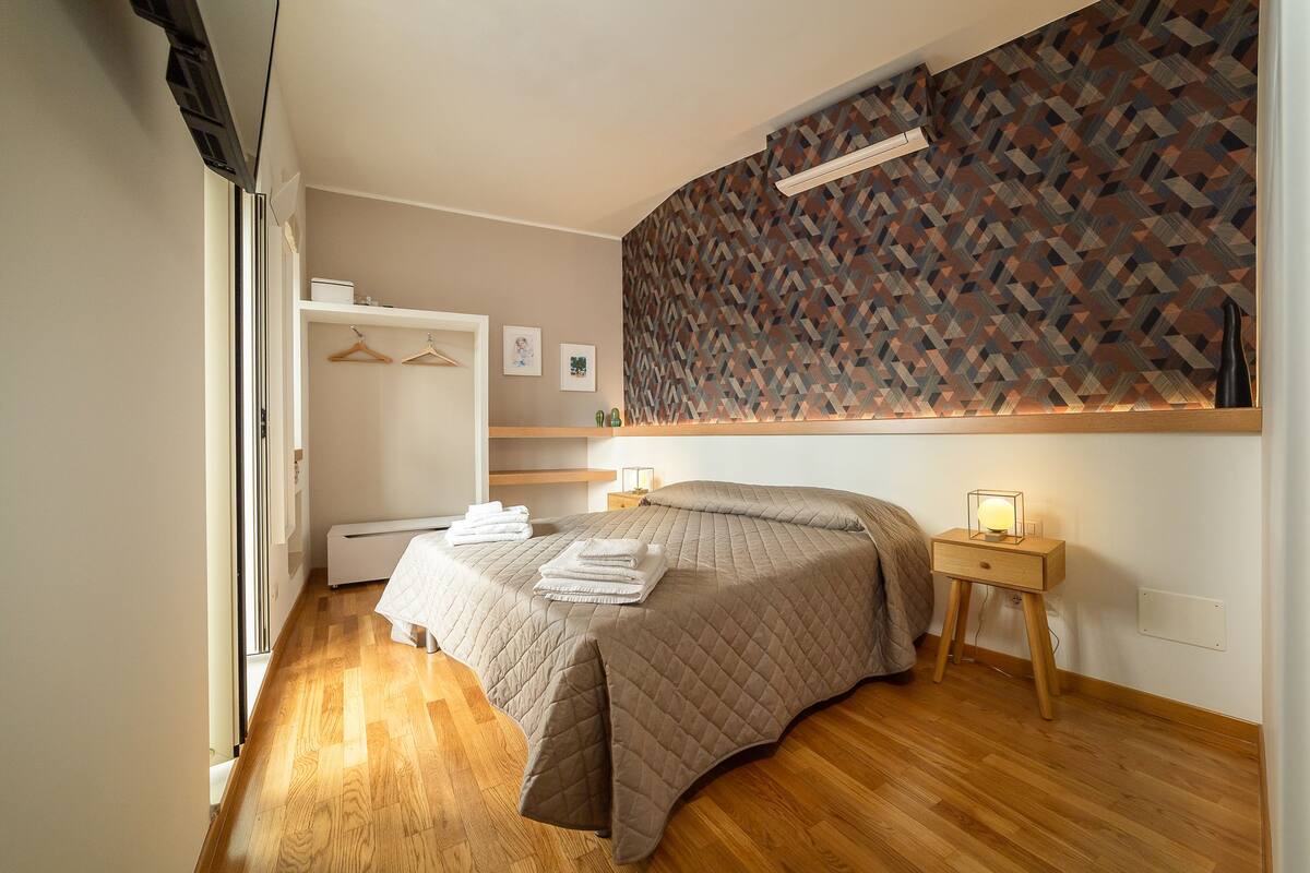 Une chambre à coucher avec un lit, une table de chevet et un mur orné d’un motif géométrique.
