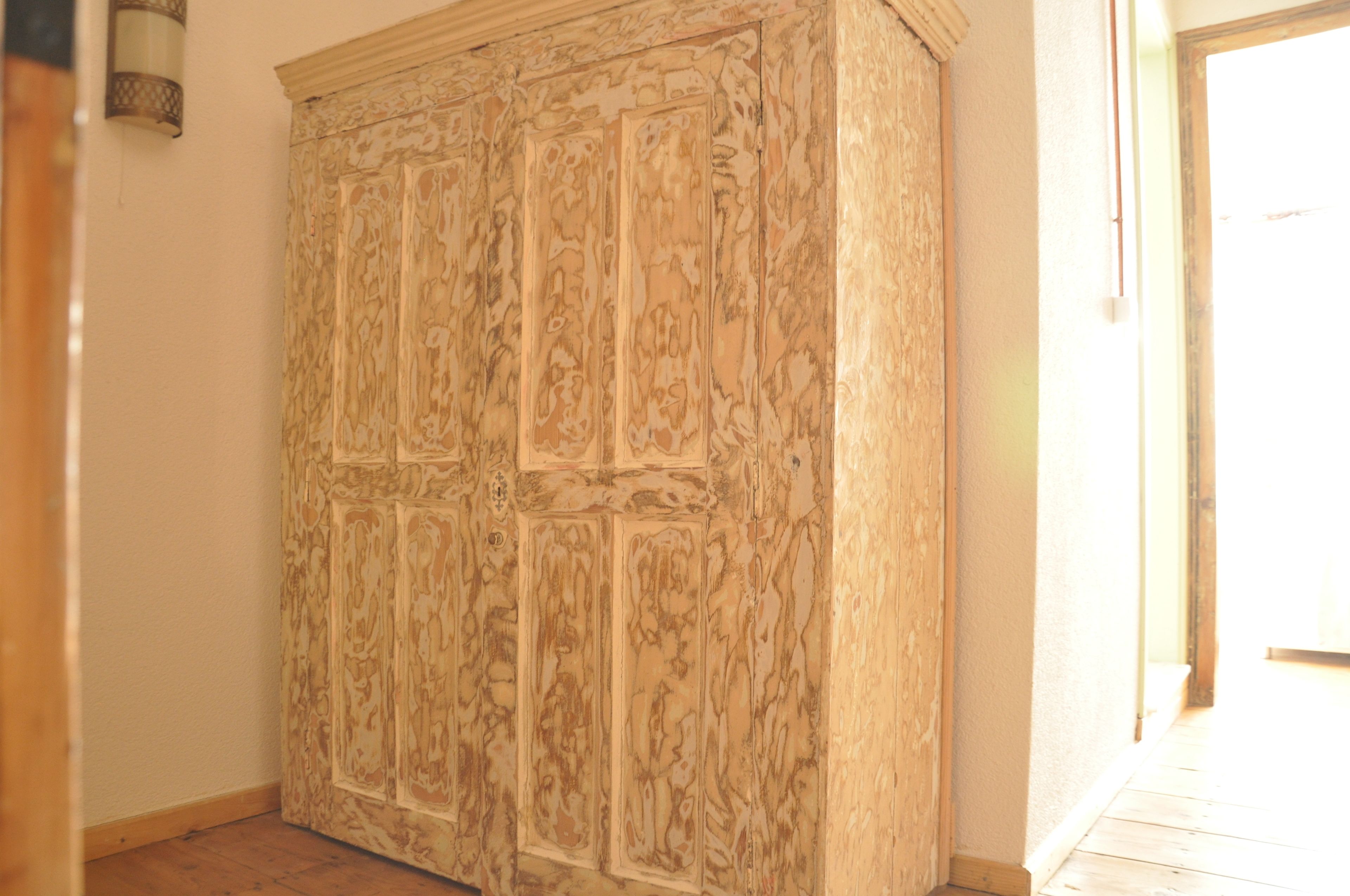A large wooden wardrobe with intricate carvings, positioned in a hallway with a wooden floor and a light-colored wall.
