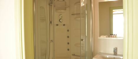 A walk-in shower with a glass door, a sink with a mirror above it, and a shelf with toiletries.