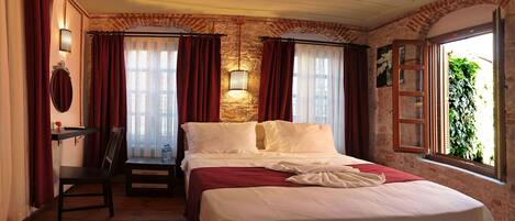 Une chambre d’hôtel avec un lit, un bureau et une chaise. Il y a une fenêtre avec des rideaux et une vue sur la verdure à l’extérieur.
