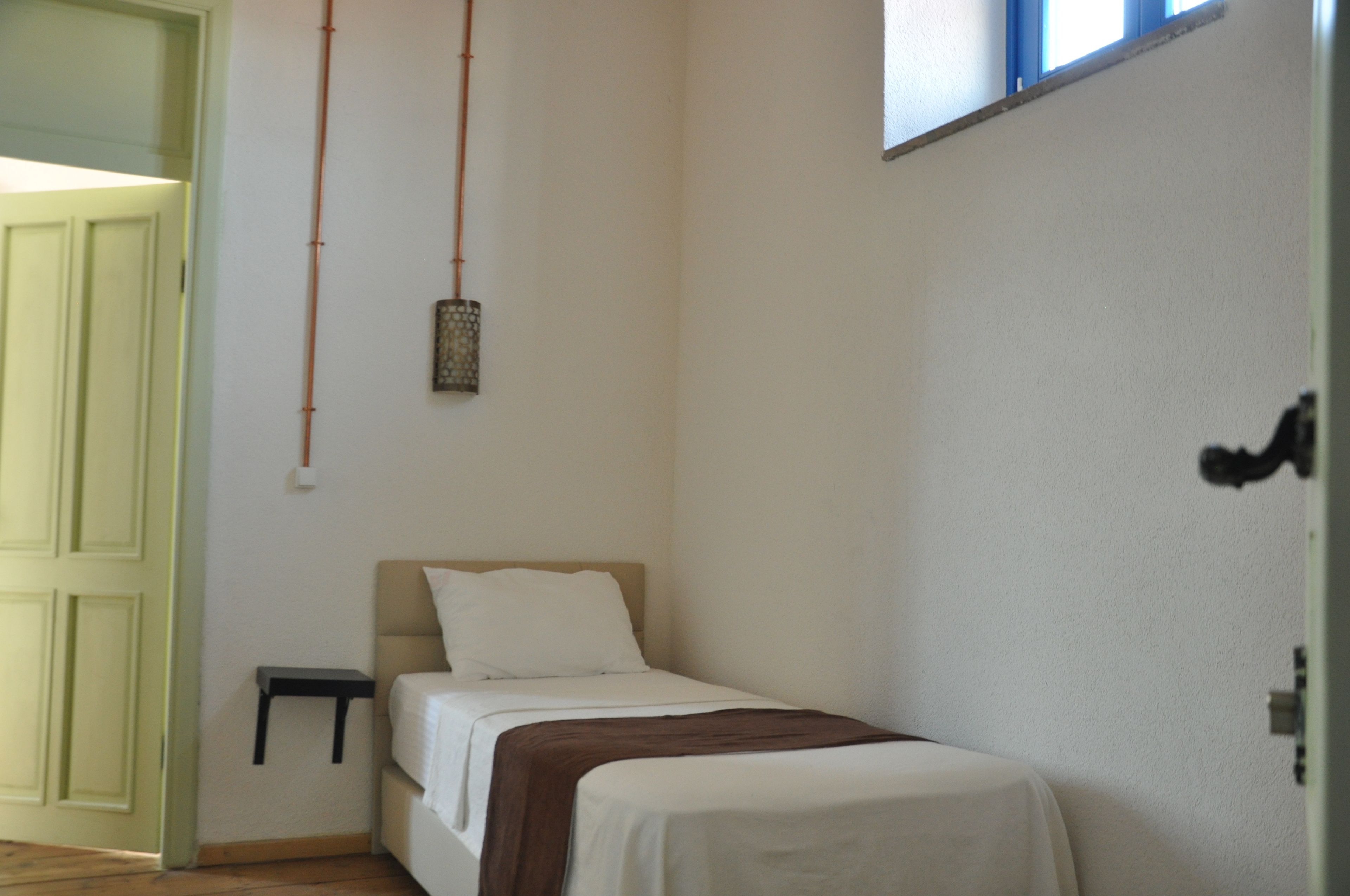 A small, neatly arranged bedroom with a single bed, a bedside table, and a hanging light fixture.