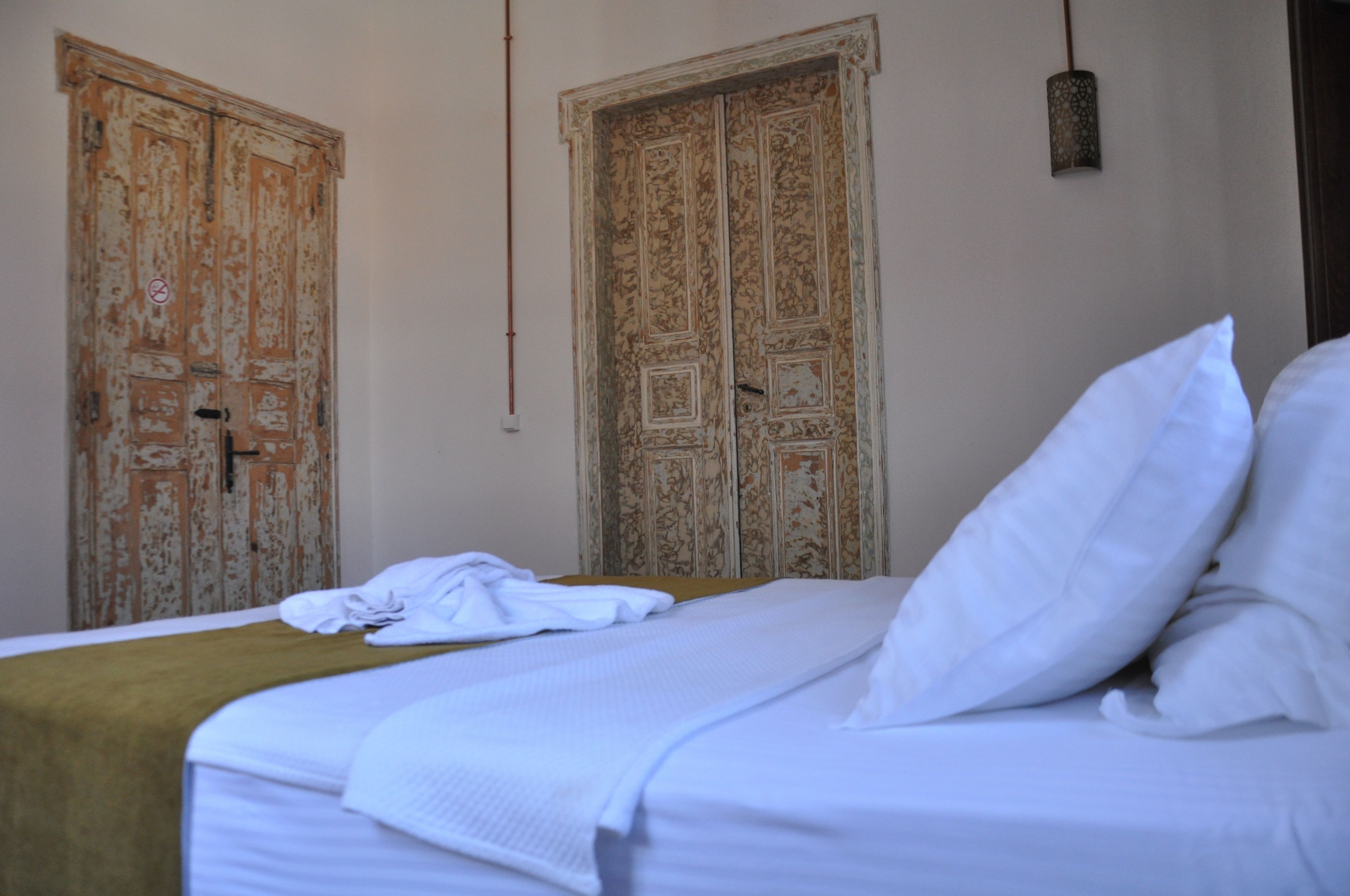 A hotel room with a bed, a wooden door, and a hanging light fixture.