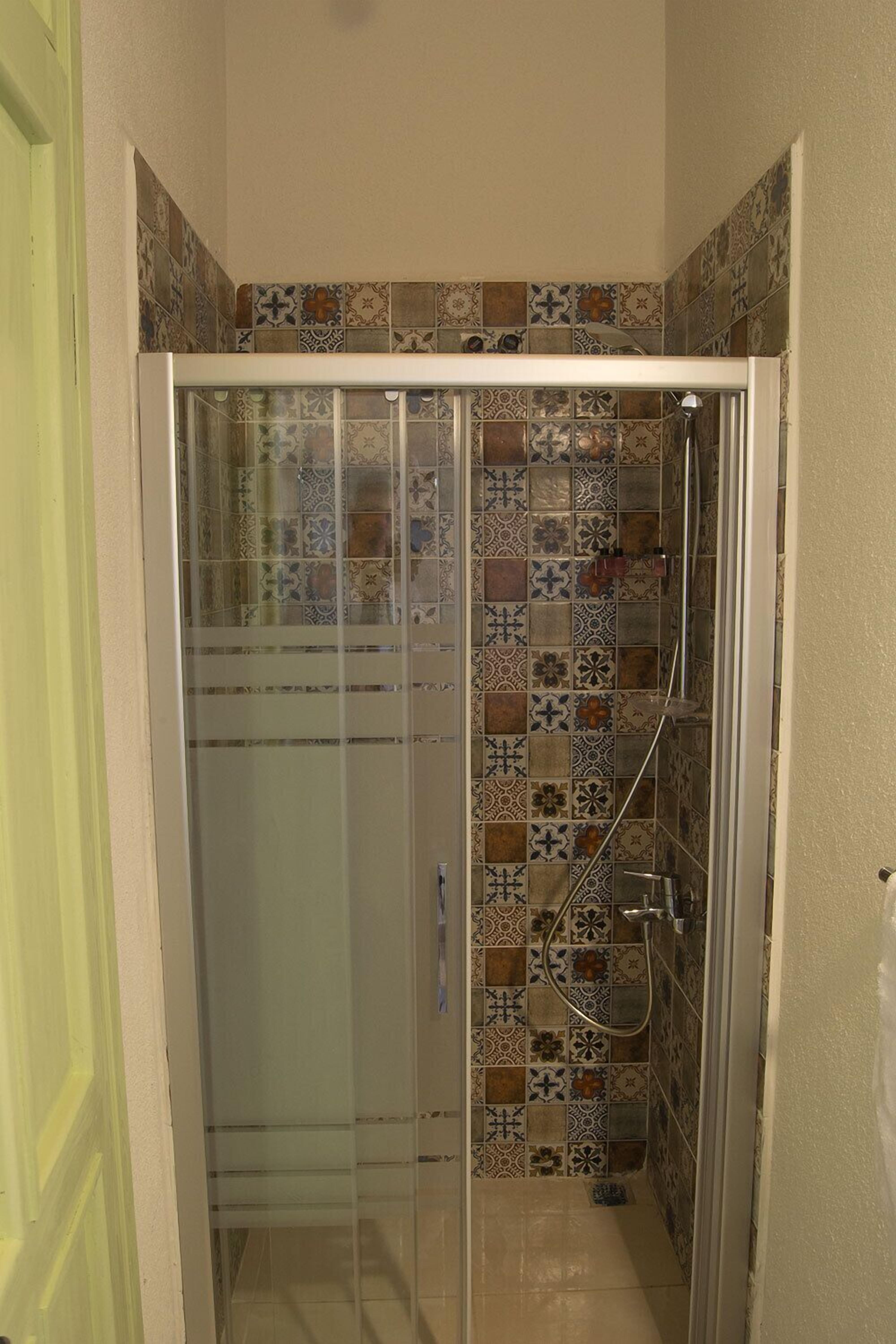 Ducha con cerramiento de vidrio y pared revestida con diversos diseños.