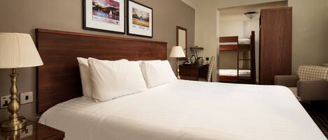 A hotel room with a large bed, two bedside tables, a lamp, a mirror, and a bunk bed in the background.