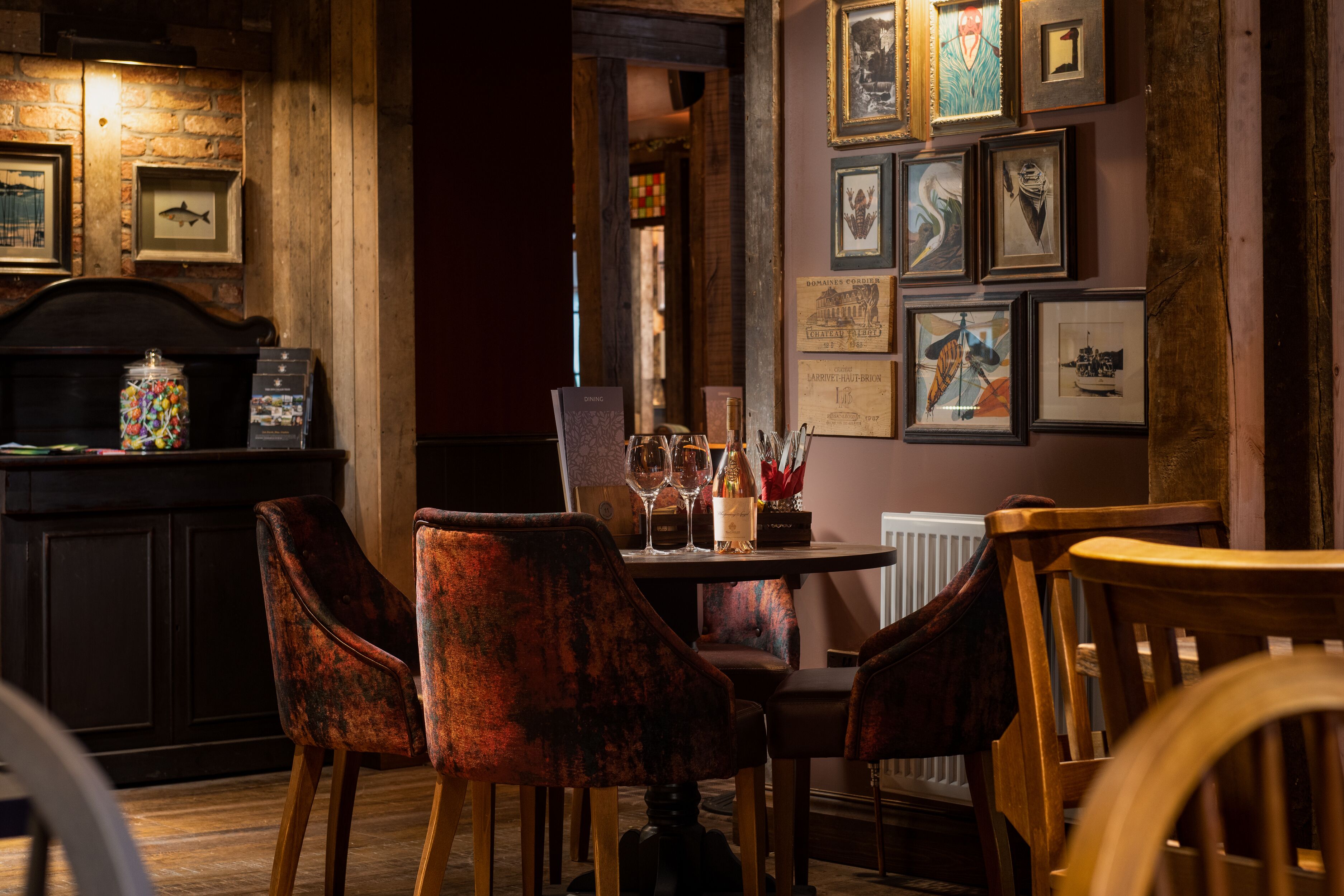 A dining area with a wooden table set for four, surrounded by upholstered chairs. There are framed artworks on the wall and a vintage-style jukebox on the left.