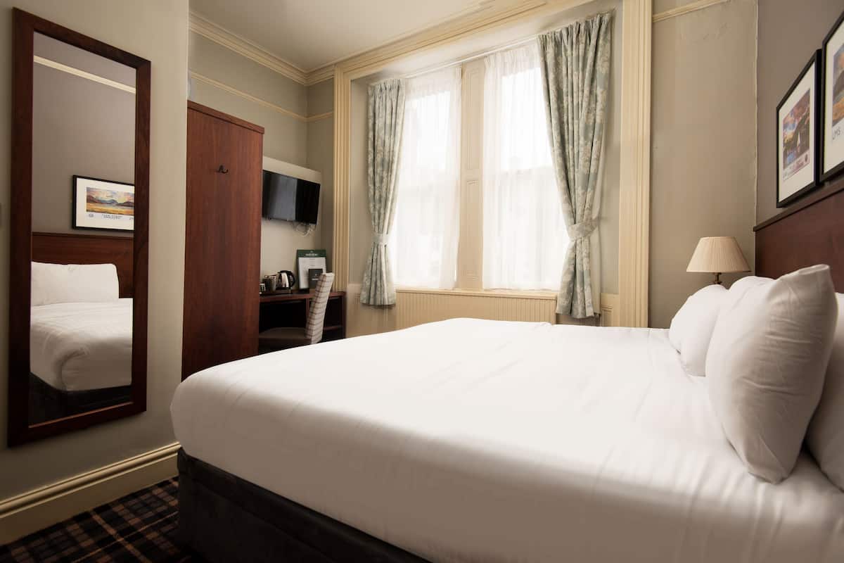 A hotel room with a large bed, a wardrobe, a television, and a window with curtains.