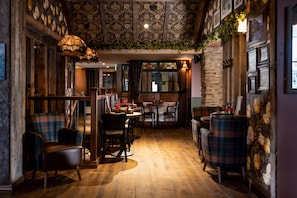 Un interior acogedor y rústico con pisos de madera, sillas de estampado escocés y una zona de comedor con pared de piedra e iluminación colgante.