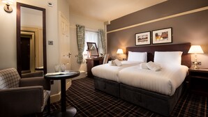 A hotel room with a bed, a chair, a table, a mirror, and a wall with two framed pictures. - The Ambleside Inn - The Inn Collection Group (Ambleside)