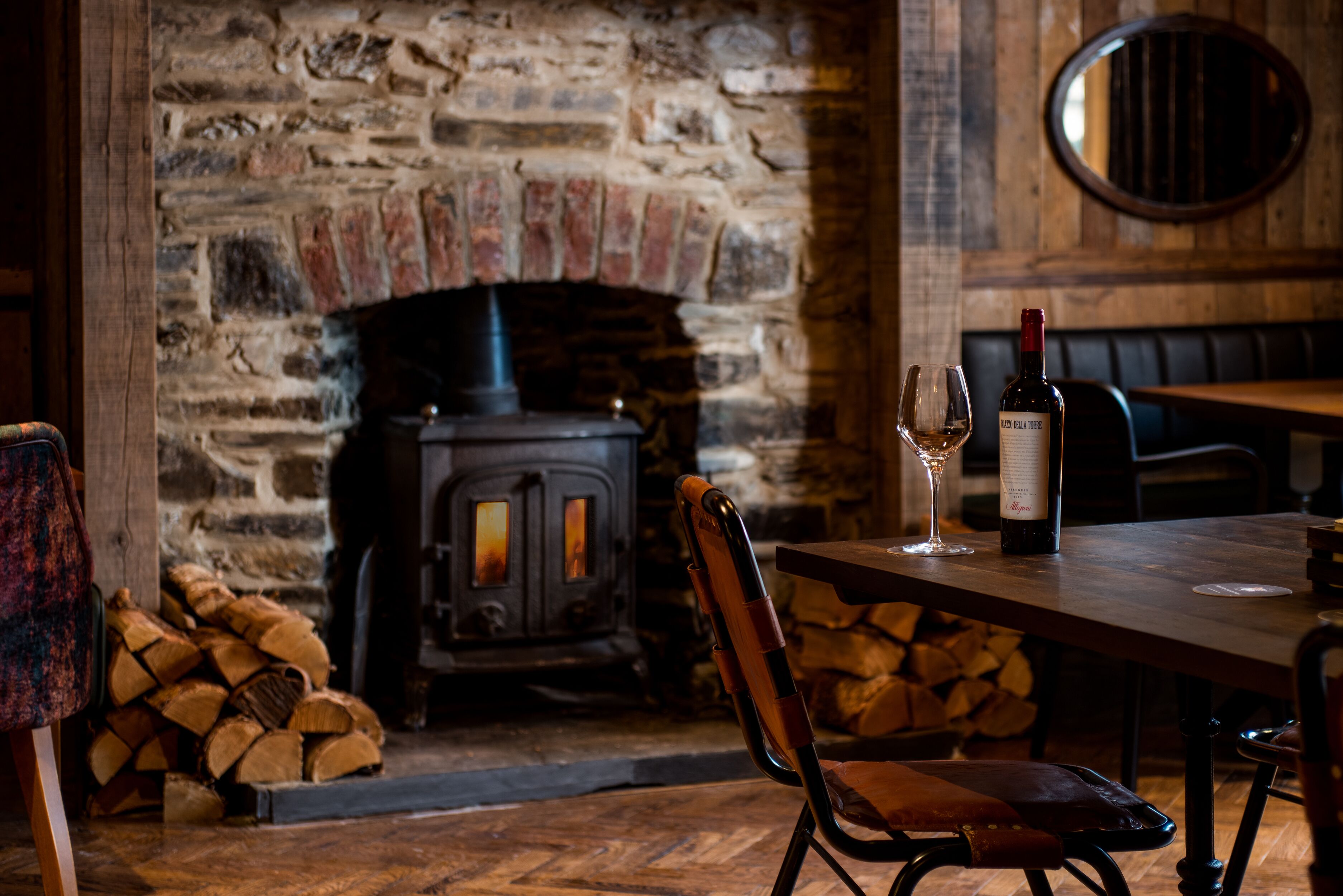 Un intérieur rustique avec une cheminée en pierre, une table avec une bouteille de vin et des verres, et un fauteuil en cuir.