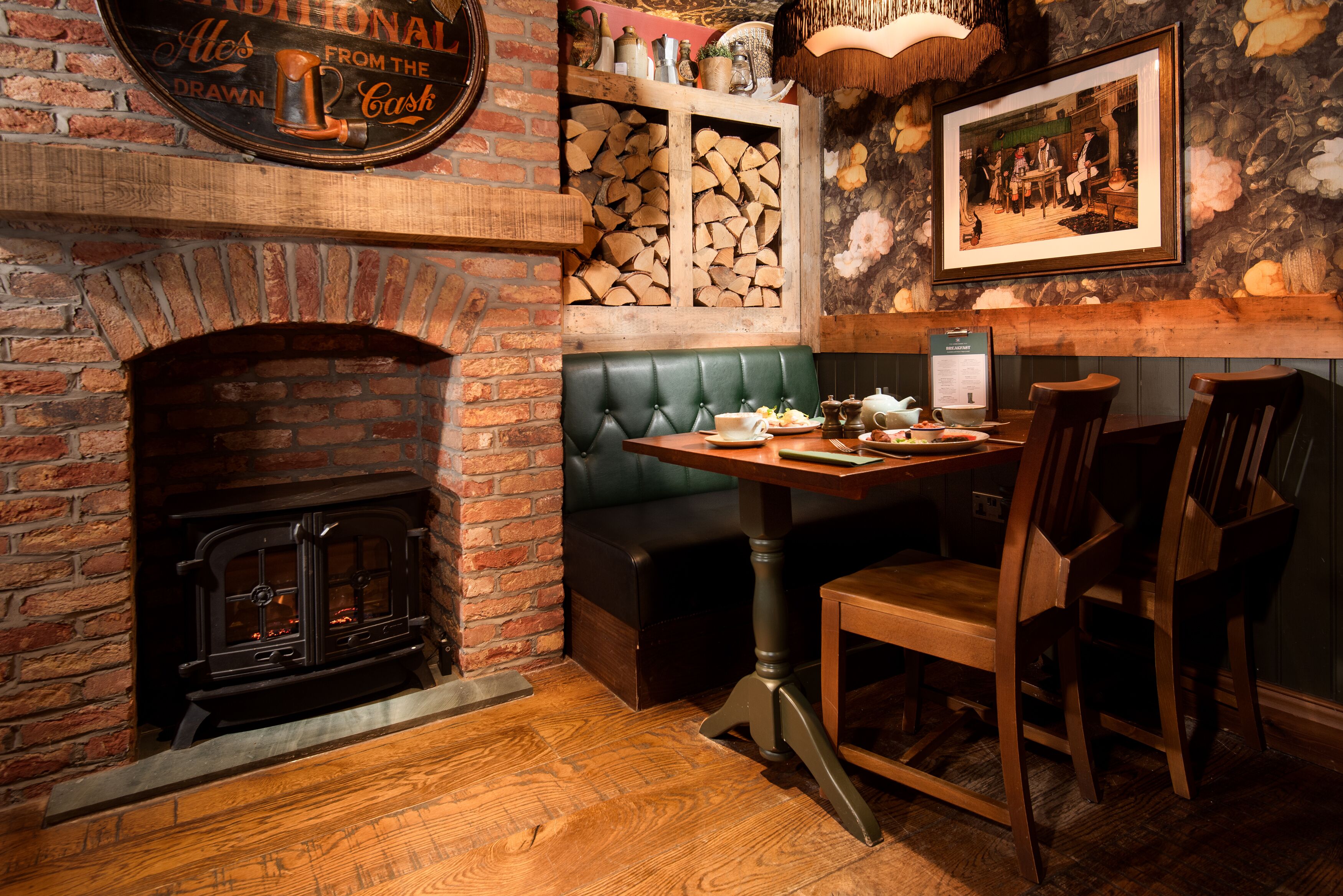 A cozy pub with a brick fireplace, a wooden table, and a green booth.