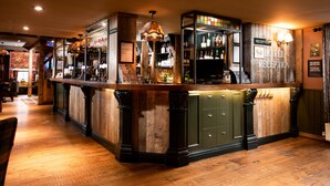 Un área de recepción con un mostrador de madera, un bar con estantes llenos de botellas y un cartel que dice 'Hotel Reception'.