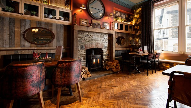 A cozy room with a stone fireplace, wooden furniture, and a large window.