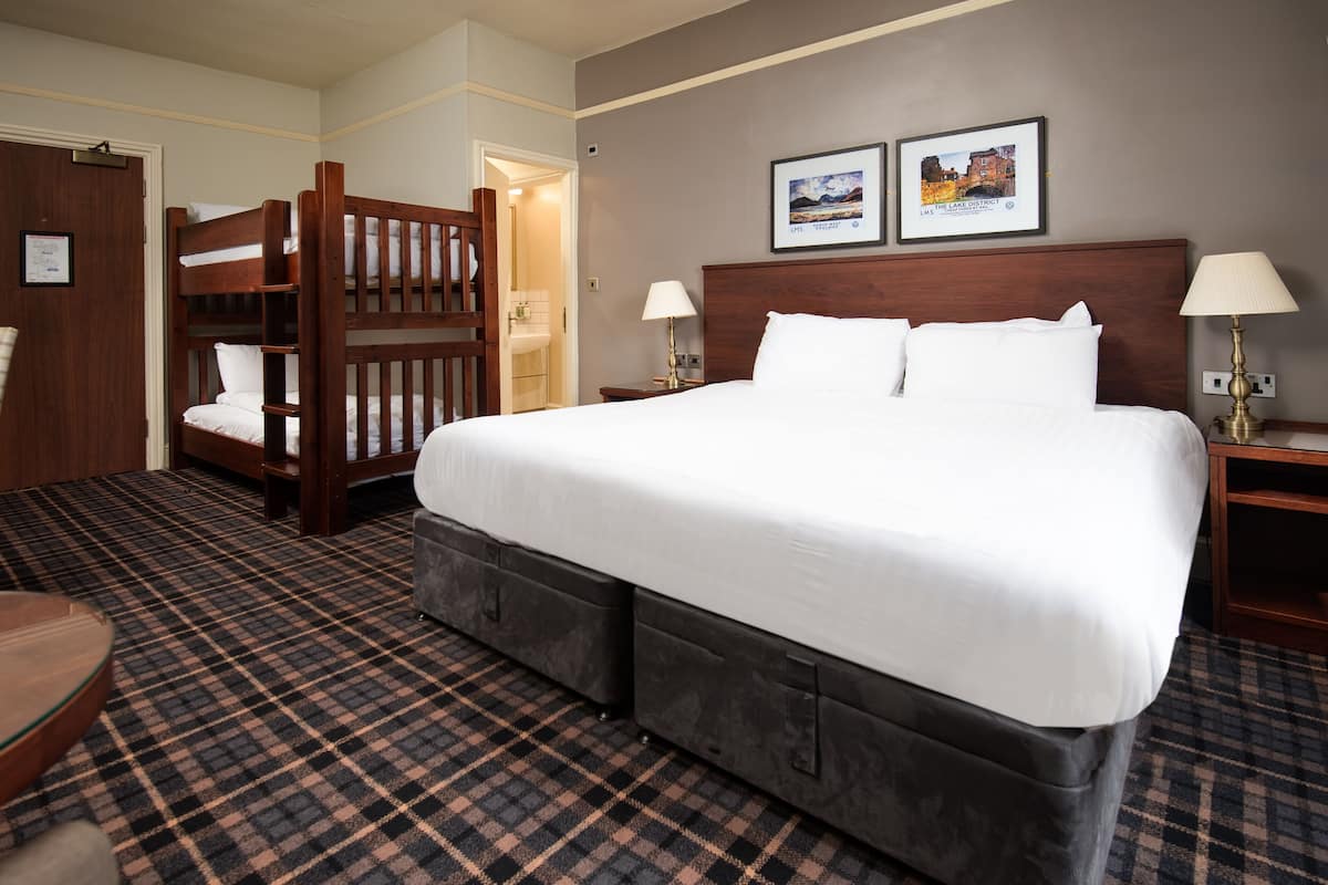 A hotel room with a large bed, a wooden bunk bed, a checkered carpet, and two framed pictures on the wall.