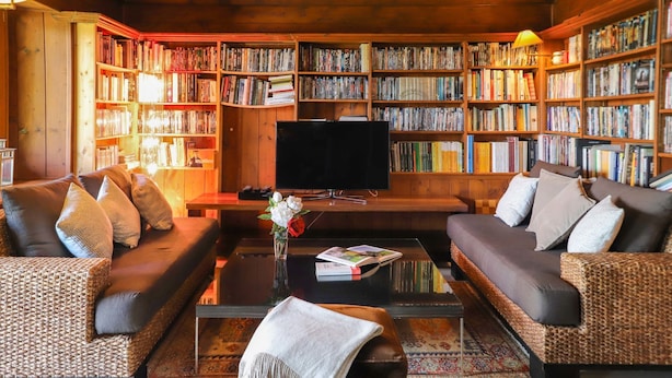 Uma sala de estar aconchegante com uma grande estante de livros, dois sofás, uma mesa de centro e uma televisão.