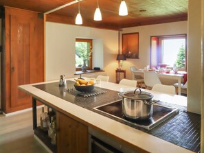 Une cuisine dotée d’un îlot central, un coin repas avec une table et des chaises, et une vue sur l’extérieur grâce à une fenêtre.