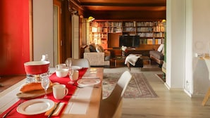 Uma sala de jantar com uma mesa vermelha posta para quatro pessoas, uma mesa de madeira e um sofá ao fundo.