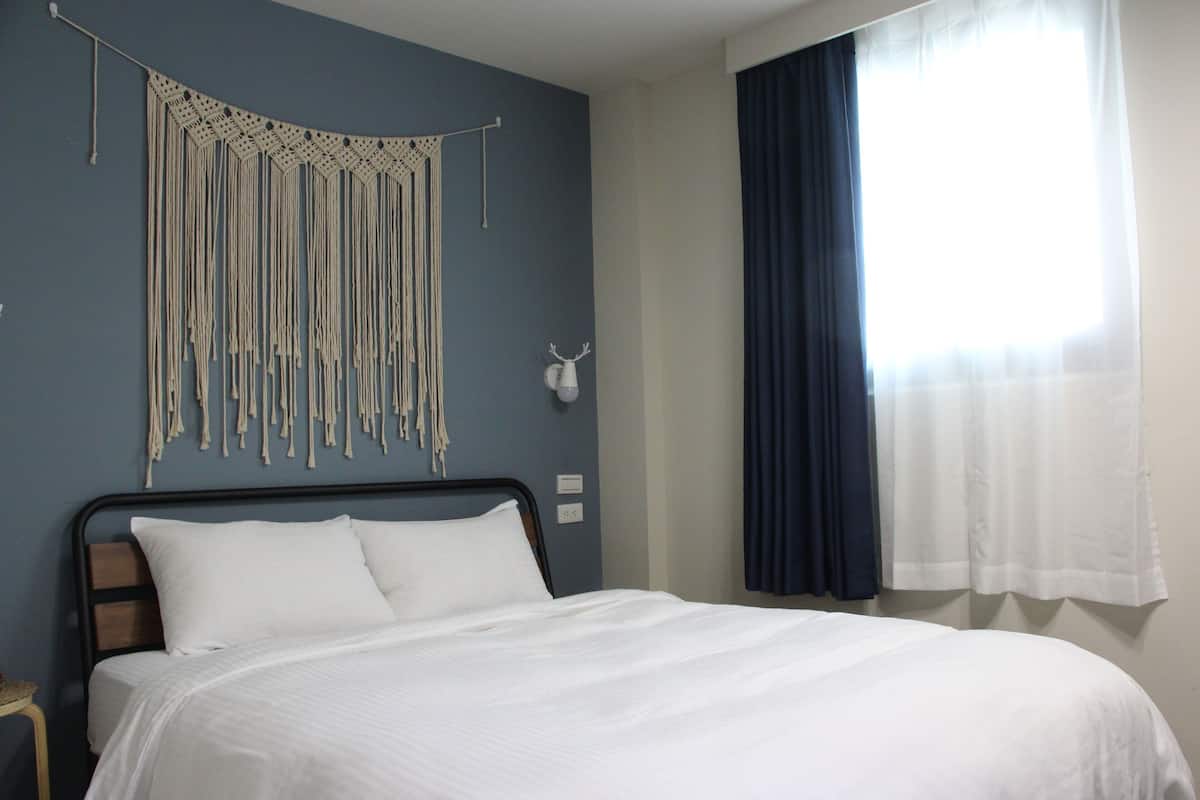 Un dormitorio con cama, un tapiz en la pared y una ventana con cortinas.