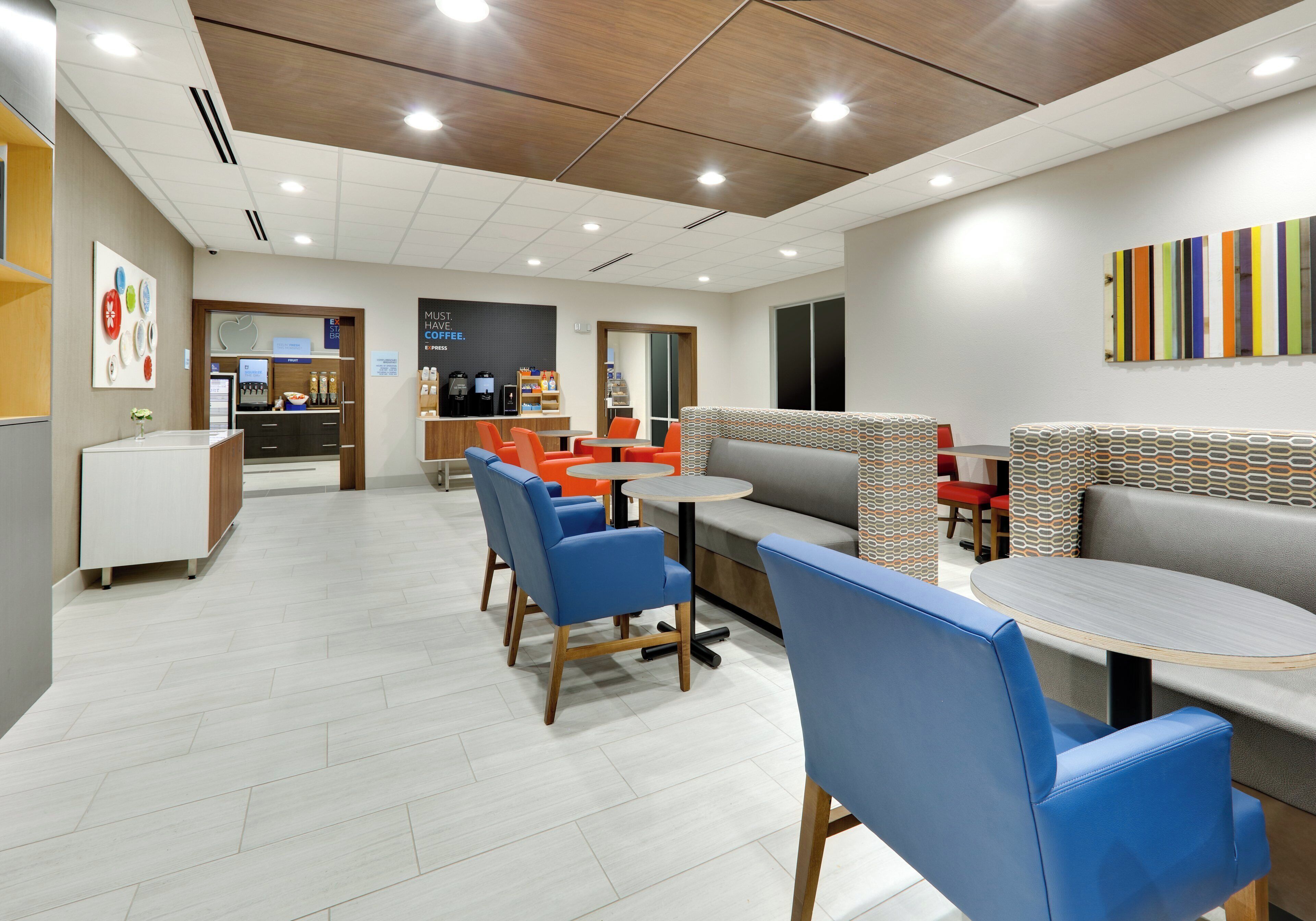 A modern cafe with seating arrangements, a coffee station, and a wall with a colorful abstract art piece.