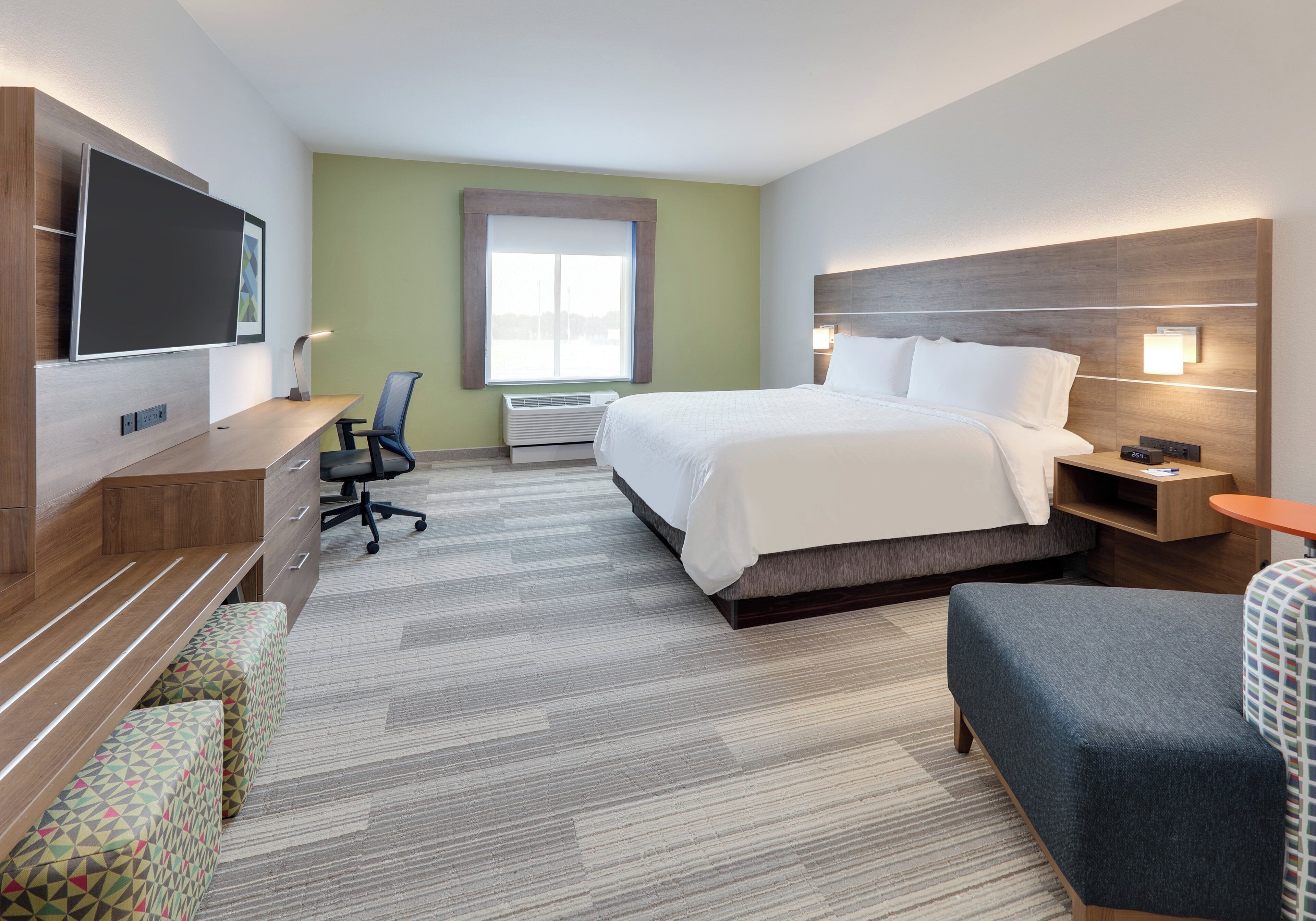 A hotel room with a bed, bedside tables, a desk with a chair, a television, and a window.