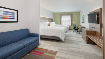 Quarto de hotel com sofá azul, duas camas, televisão, escrivaninha e tapete colorido.